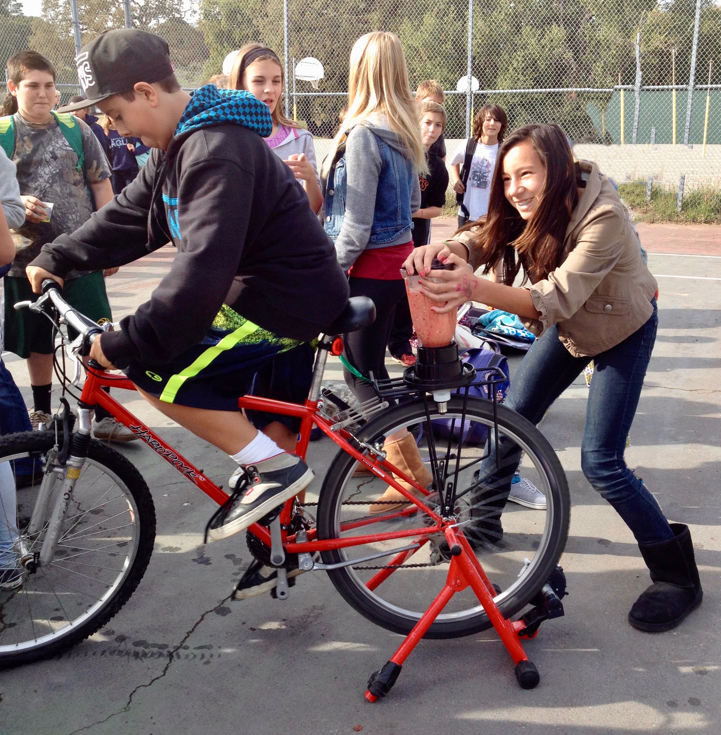 A girl holds onto a blender attached to the back of a stationary bike