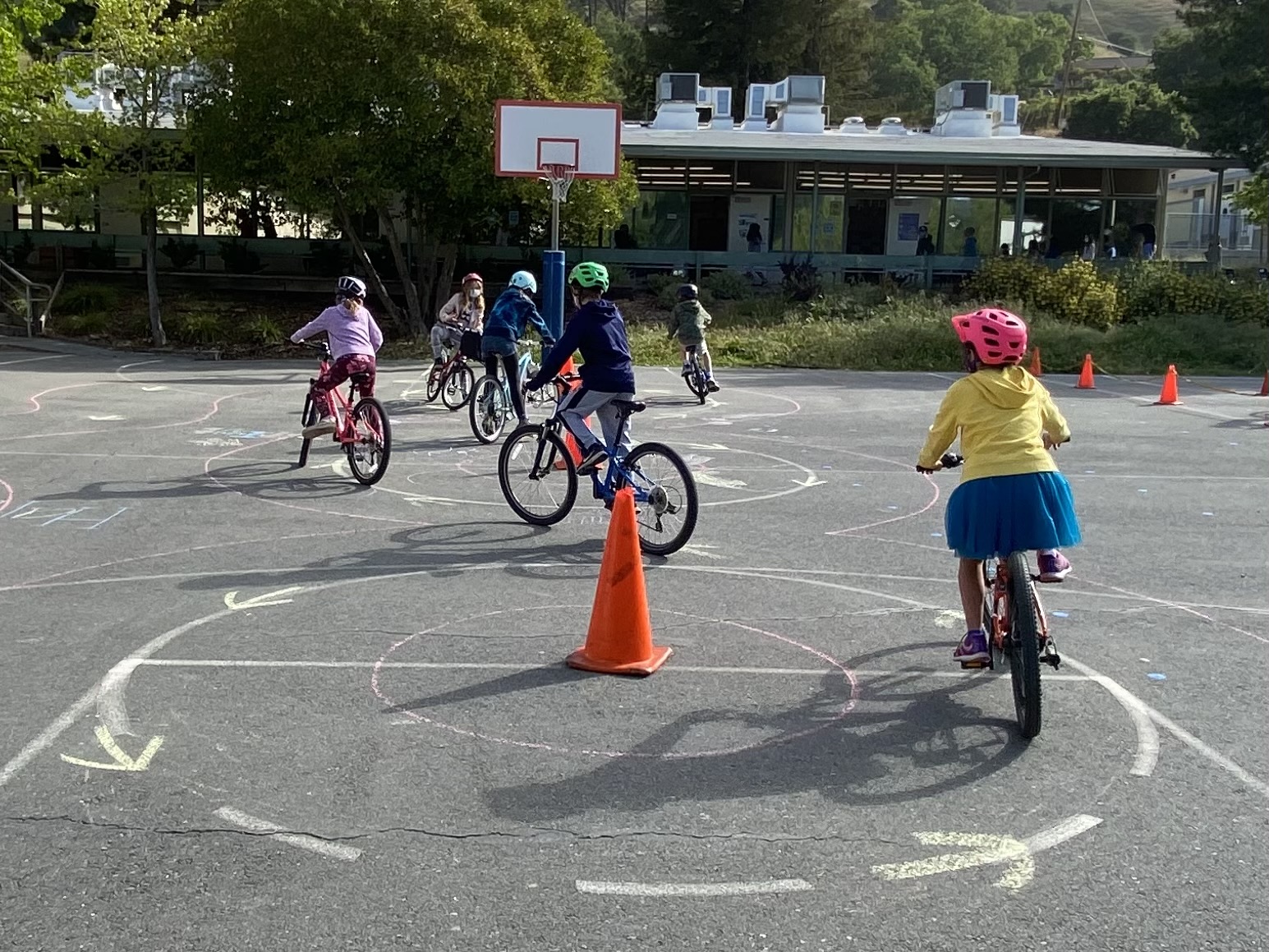 Children ride bicycles around a path marked with chalk