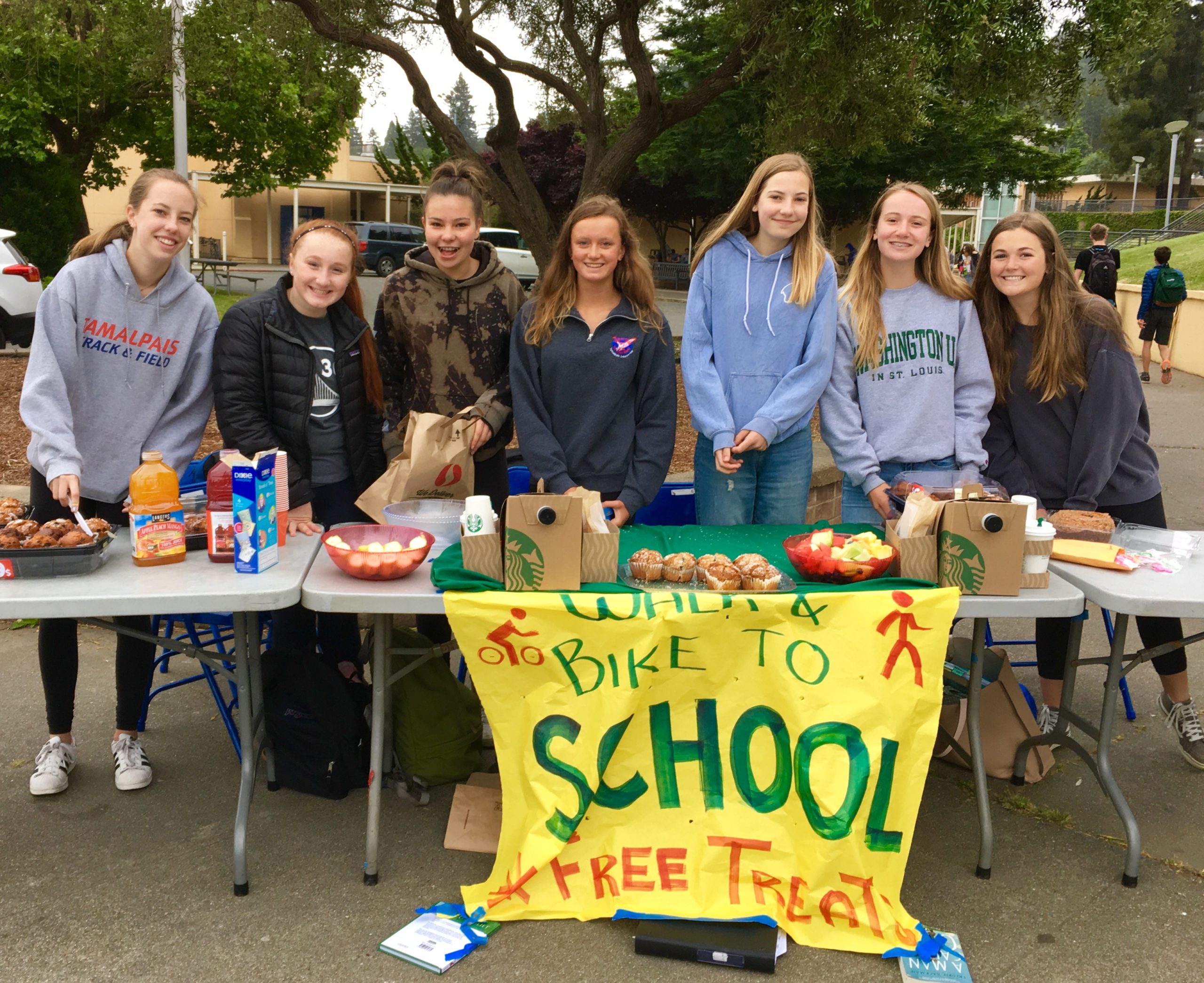 Students stand in front of a table with snacks and a sign for Walk & Bike to School Day