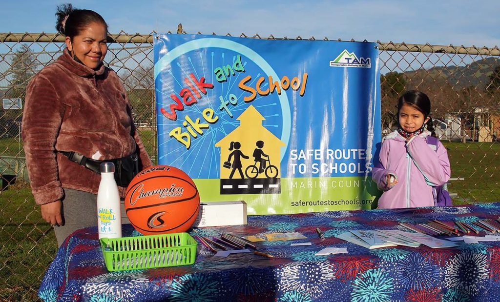 A woman and a child stand in front of a banner: Walk and Bike to School