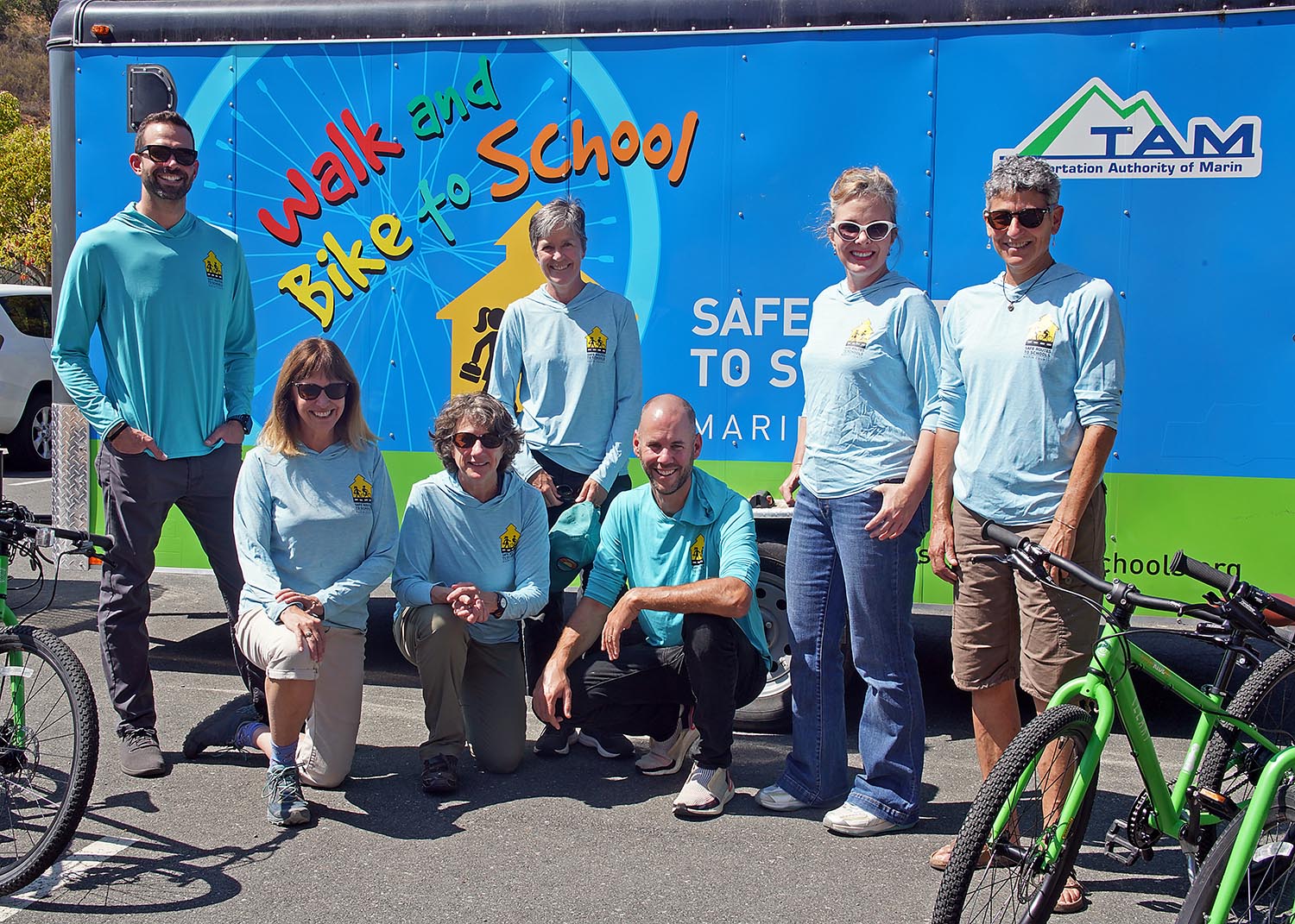 Safe Routes Staff stand with bikes in front of a trailer that reads, "Walk & Bike to School"